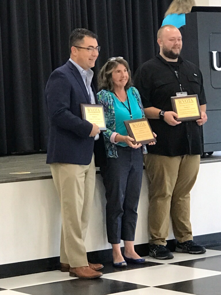 Three award winners standing together holding award plaques